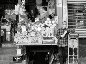 Produce seller with his sidewalk stand in Chinatown, New York, in front of store