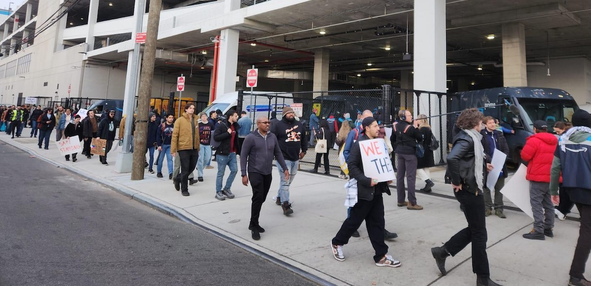 About 25 people walk along a sidewalk, some carrying signs.