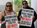 Two black women in sunglasses, one with a headscarf, hold signs saying ‘More work, less pay, NO WAY’
