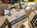 A pile of Amazon boxes is shown with workers small in the background