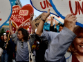 Protesters crowd towards the camera with heart-shaped signs saying “workers unite” and “hands off our postal service”